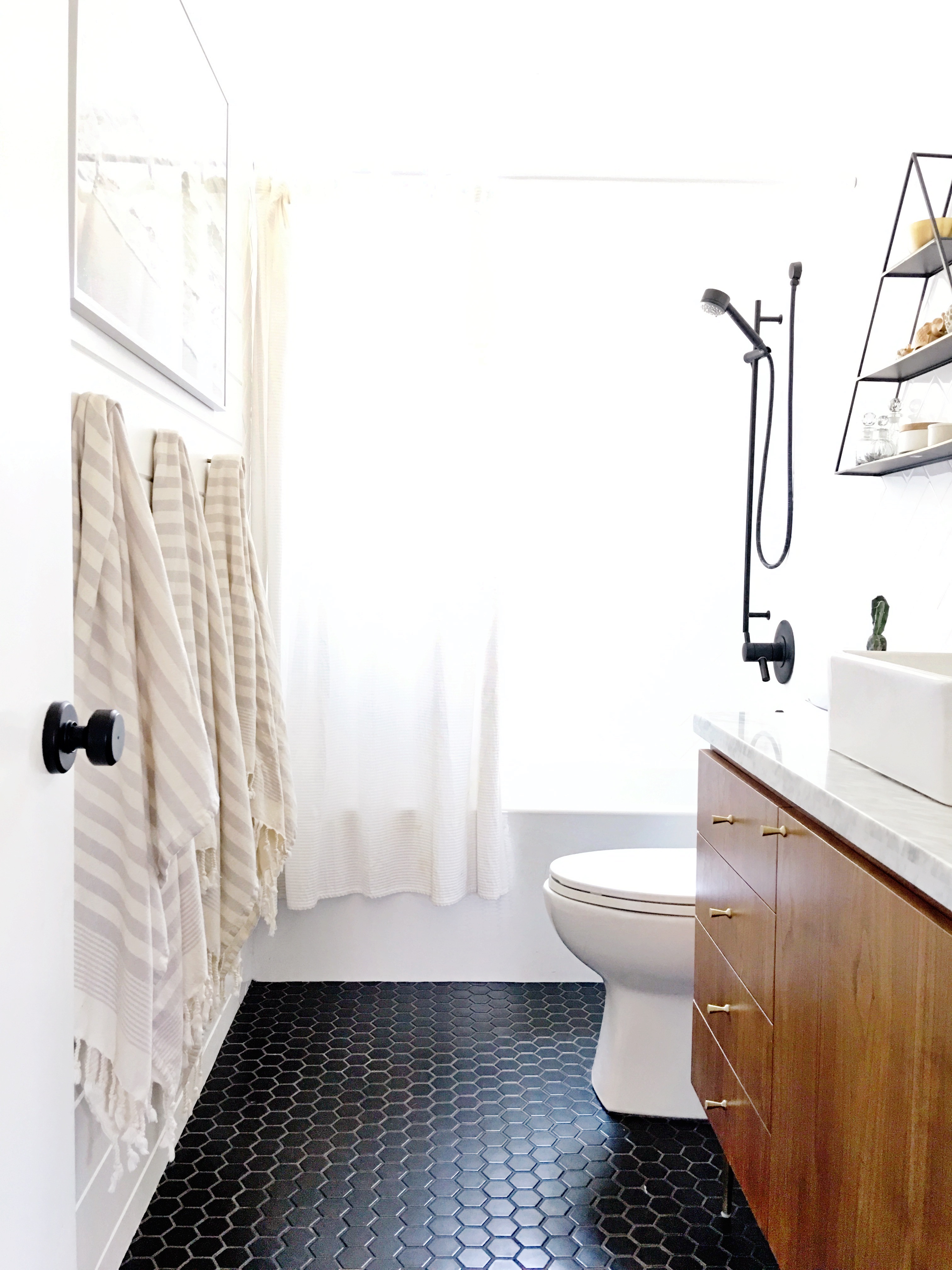 Walnut bathroom vanity with gold hardware, black floors, white walls